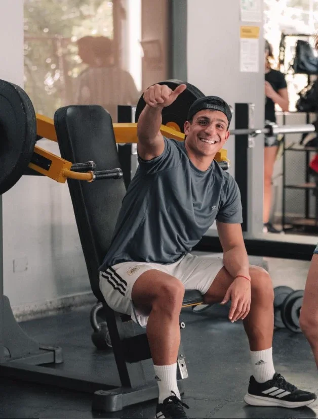 Socio sonriendo con el pulgar arriba, sentado en una máquina del gimnasio